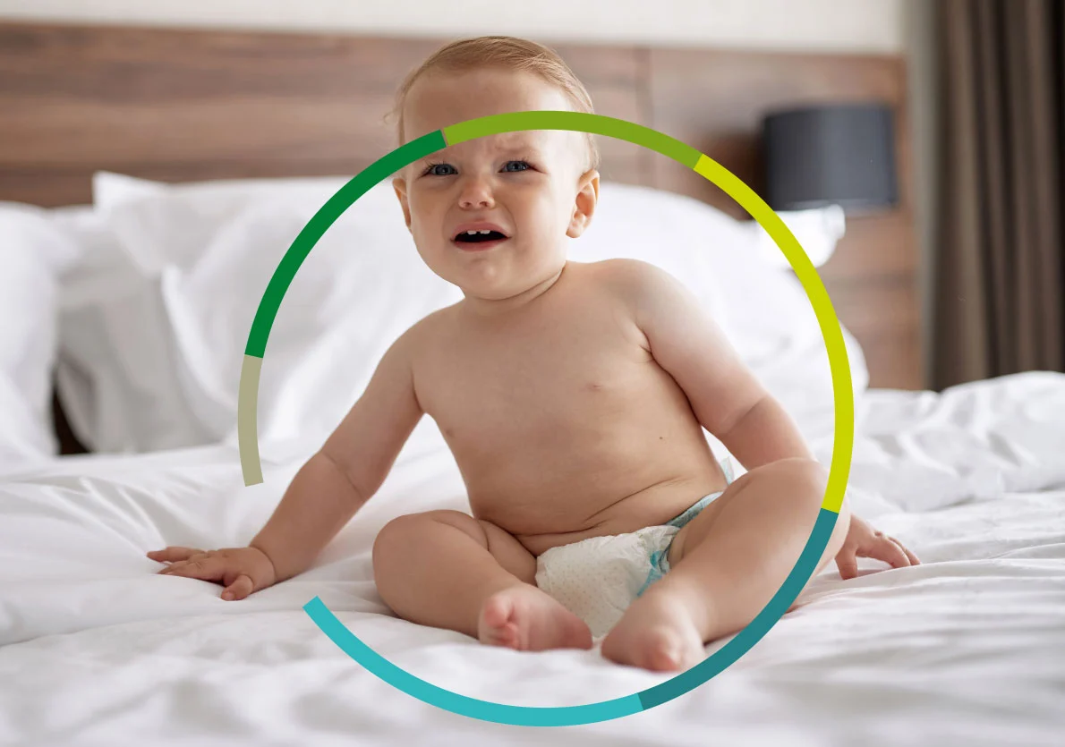 Baby sitzt mit Windel auf dem Bett